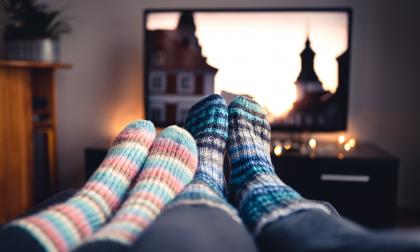 Couple with socks and woolen stockings watching movies or series on tv in winter. Woman and man sitting or lying together on sofa couch in home living room using online streaming service in television